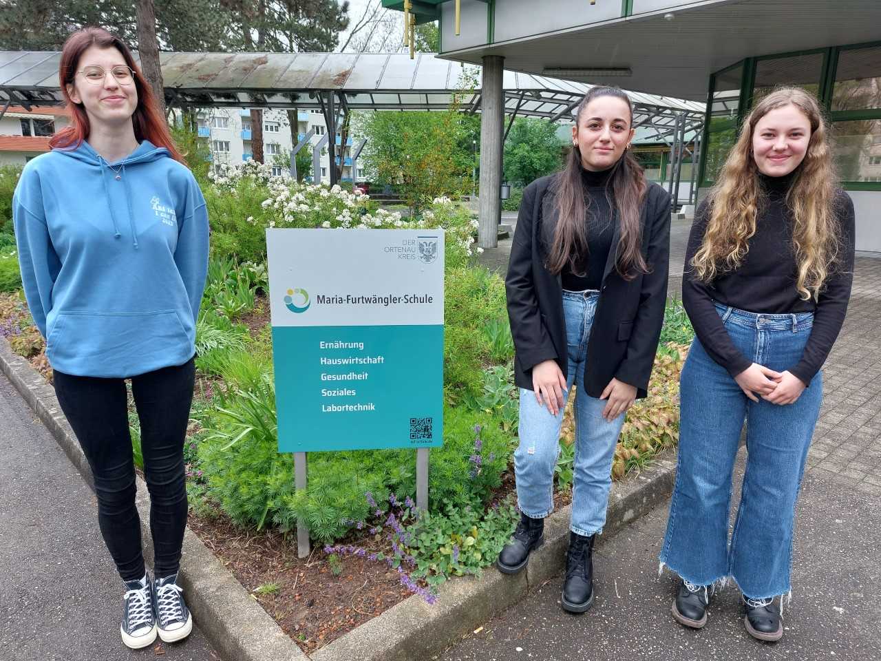 Die drei Schülerinnen aus dem Artikel vor dem Schild zur Maria-Furtwängler-Schule